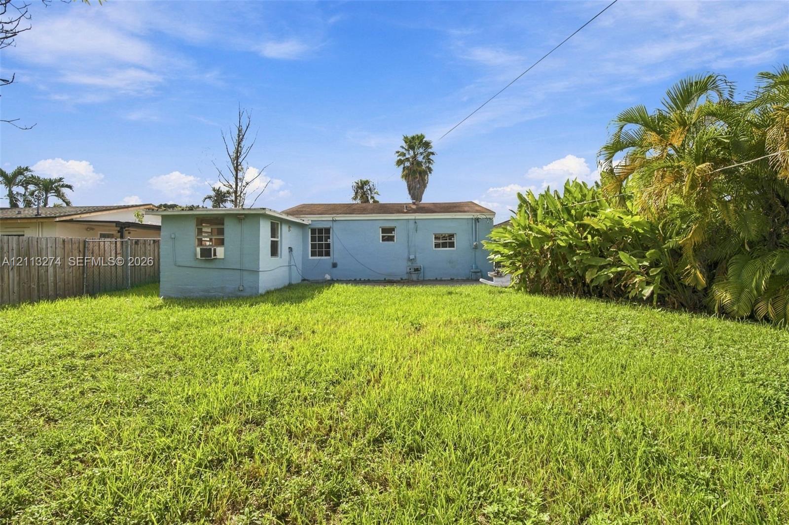 Expansive backyard featuring a grass lawn, perimeter wood fencing, and mature landscaping