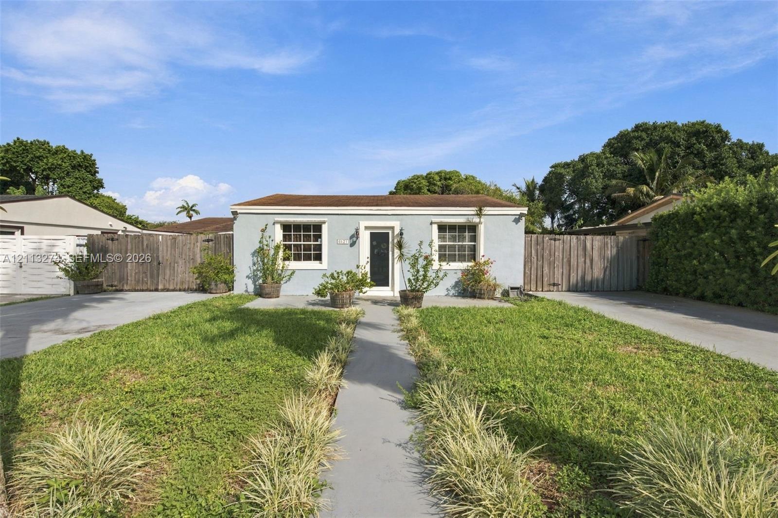 Single-story residence featuring a light-toned stucco exterior, multi-pane windows, a centered glass-panel front door, and flanking wood-plank fencing Single-story residence featuring a light-toned stucco exterior, multi-pane windows, a centered glass-panel front door, and flanking wood-plank fencing