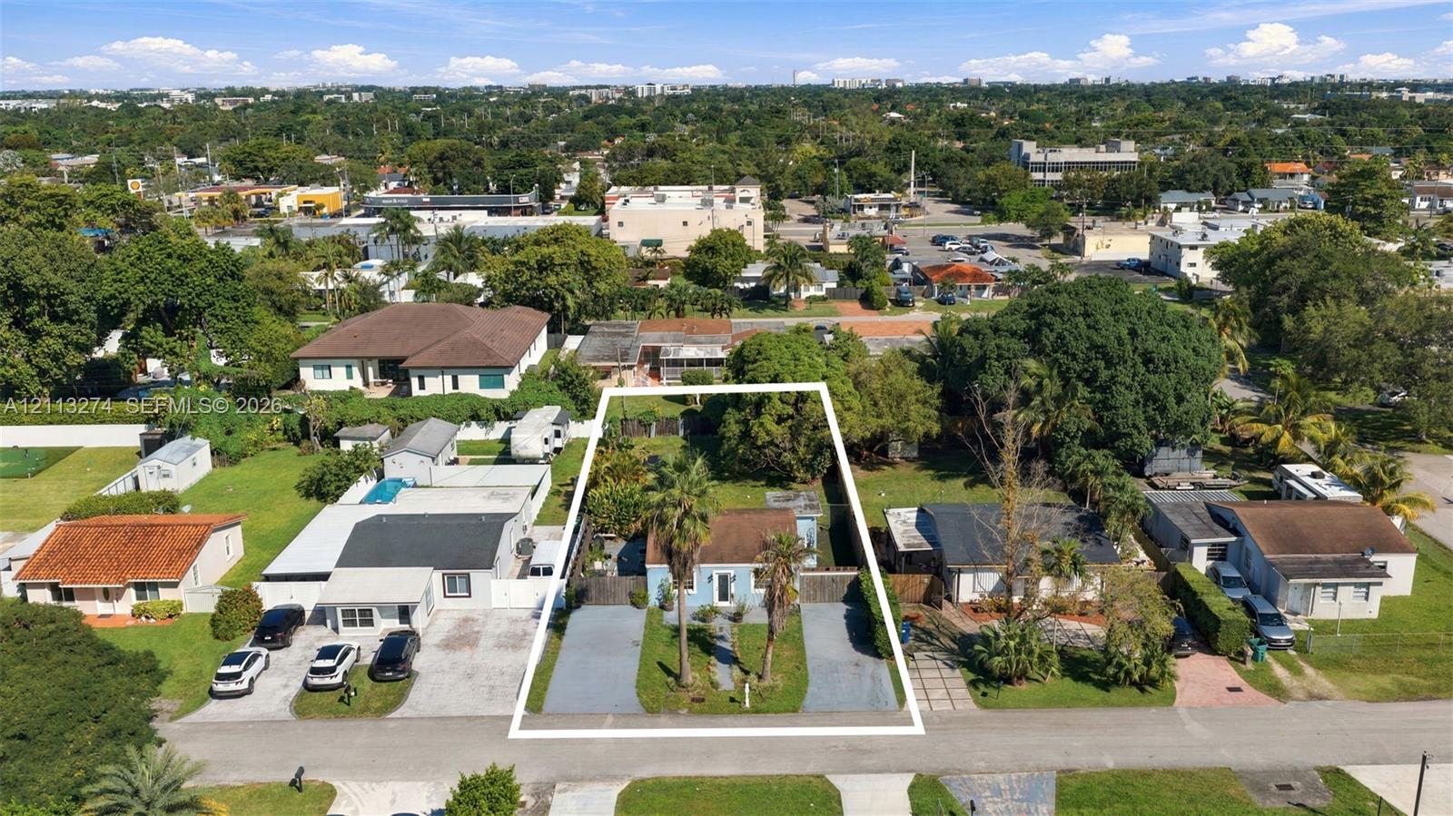 Aerial perspective of a detached property featuring dual paved driveways, established palms, and a fenced rear perimeter Aerial perspective of a detached property featuring dual paved driveways, established palms, and a fenced rear perimeter