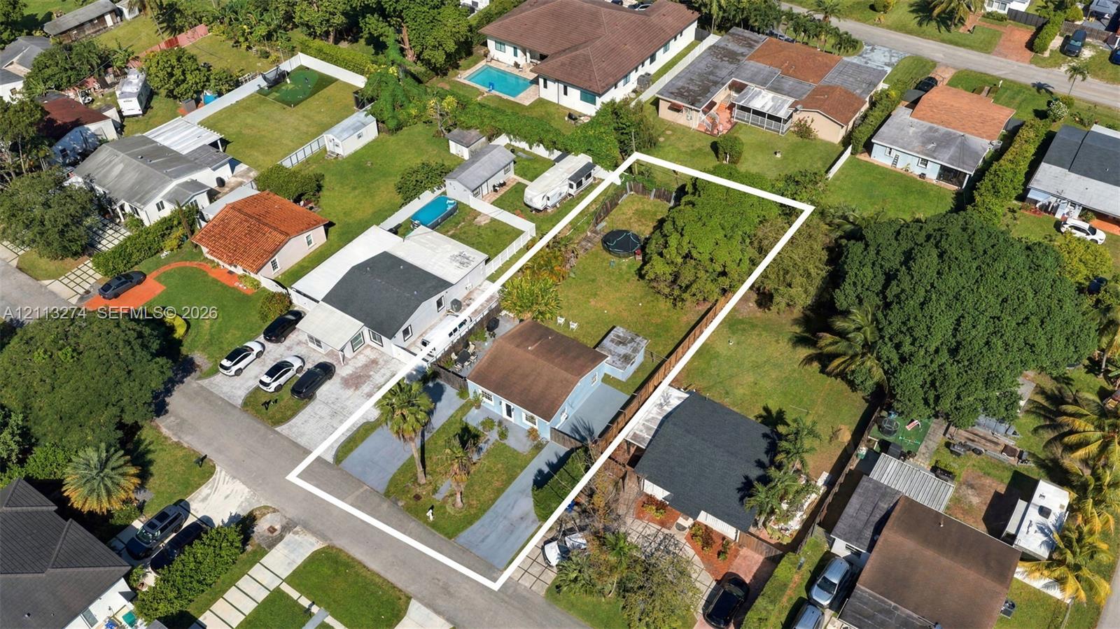 Aerial perspective of a property featuring an expansive rectangular lot, a paved driveway, and established mature trees