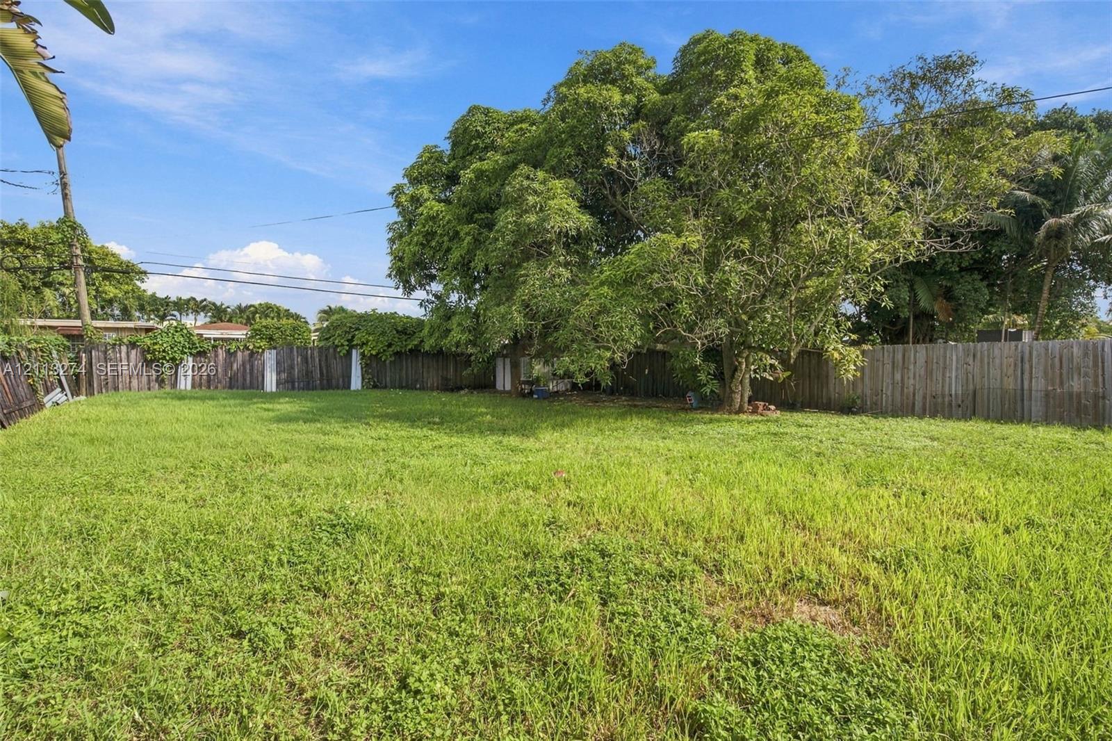 Expansive backyard featuring a large grass lawn, mature trees, and perimeter wood fencing Expansive backyard featuring a large grass lawn, mature trees, and perimeter wood fencing