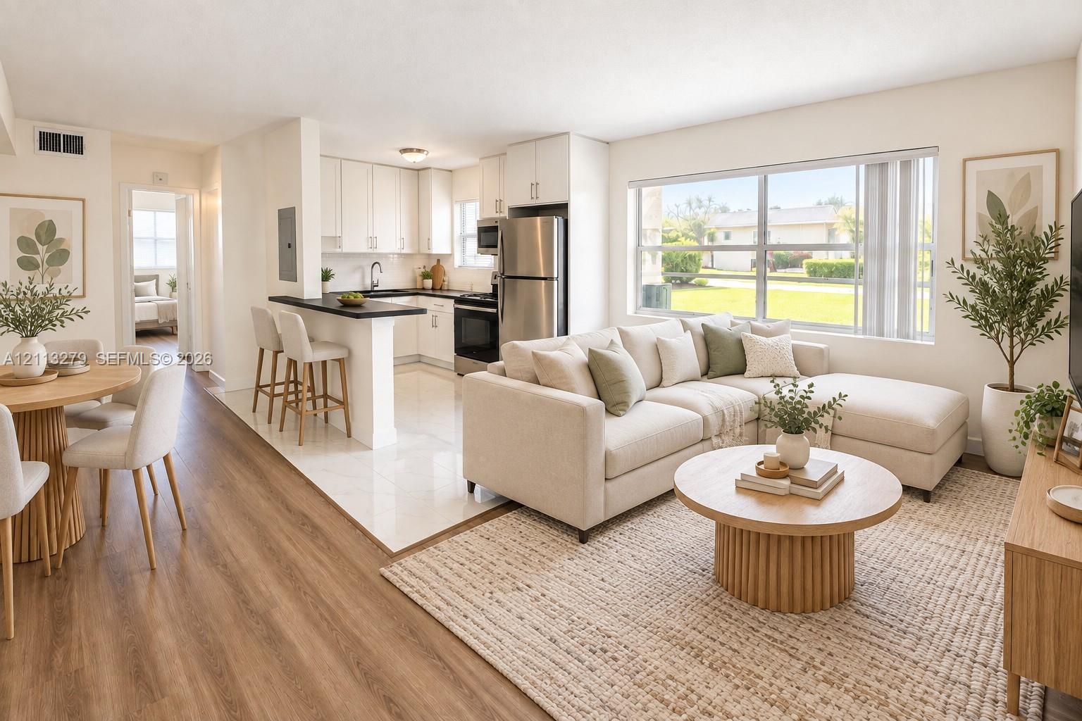 Open-concept interior featuring wood-finish flooring, white cabinetry, contrasting dark countertops, a breakfast bar, and a large picture window Open-concept interior featuring wood-finish flooring, white cabinetry, contrasting dark countertops, a breakfast bar, and a large picture window