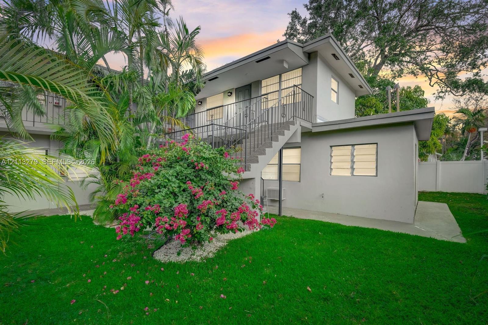 Two-story exterior featuring a metal staircase, railing, louvered windows, and a concrete patio