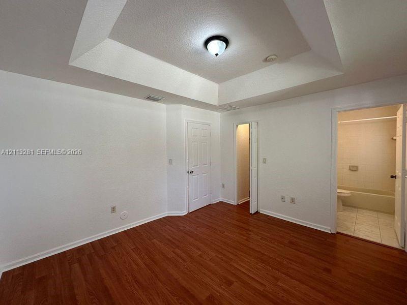 Tray ceiling with central flush-mount lighting, wood-finish flooring, and multi-panel interior doors
