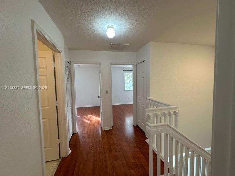 Hallway featuring wood-finish flooring, white paneled doors, ceiling-mounted light fixture, and wooden staircase railing