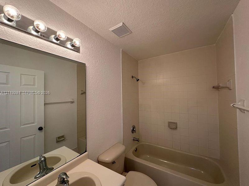 Bathroom featuring a vanity with integrated sink, large wall-mounted mirror, four-light vanity fixture, and a tiled tub-shower combination