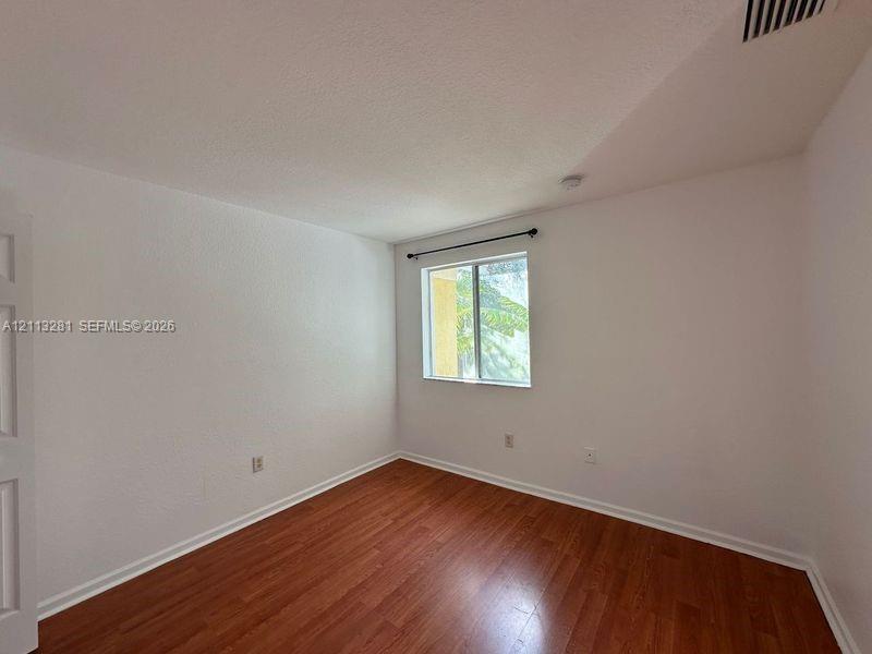 Interior space featuring wood-finish flooring, white walls, and a window with a mounted curtain rod