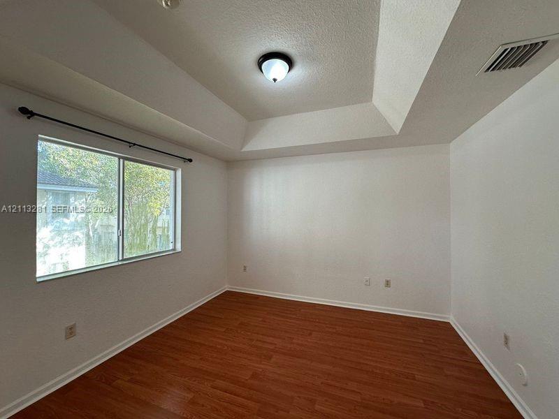 Tray ceiling, wood-finish flooring, and single-pane window with horizontal rod