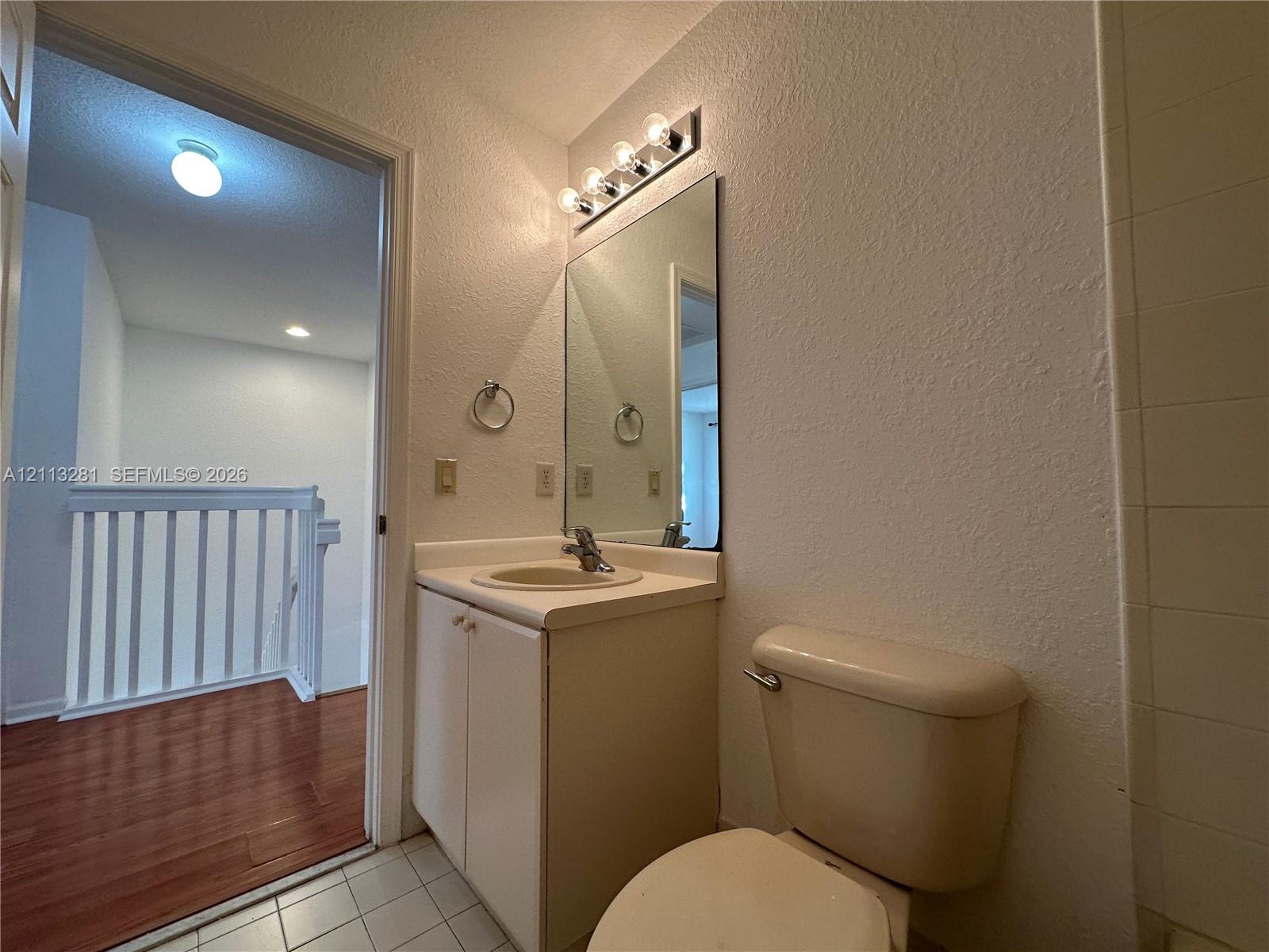 Bathroom featuring a vanity with an integrated sink, wall-mounted mirror, multi-bulb vanity light fixture, and tile flooring