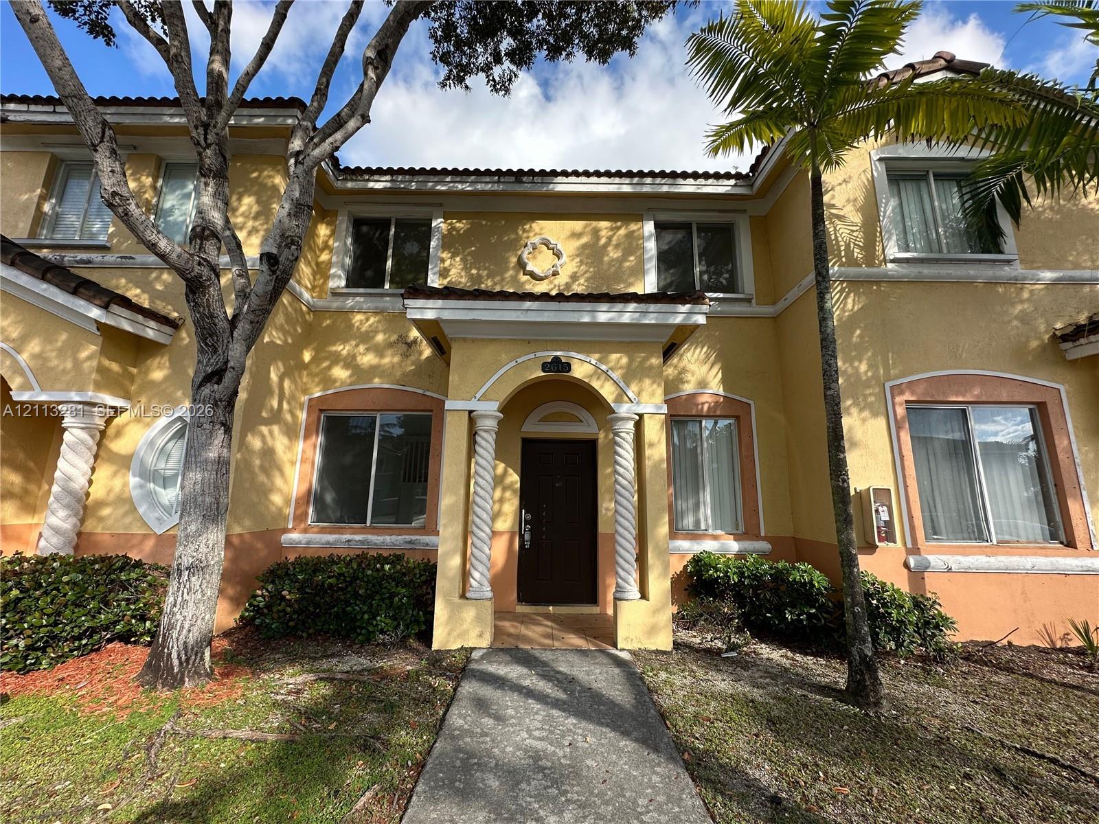 Two-story exterior featuring stucco siding, spiral columns at the entryway, decorative arch window detailing, and a tile roof