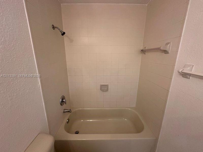 Bathtub surround featuring square ceramic tile, built-in soap dish, chrome shower head, and wall-mounted towel bars