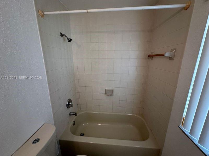Full-height square wall tile surround, built-in soap dish, porcelain bathtub, chrome shower fixture, and wall-mounted towel bar