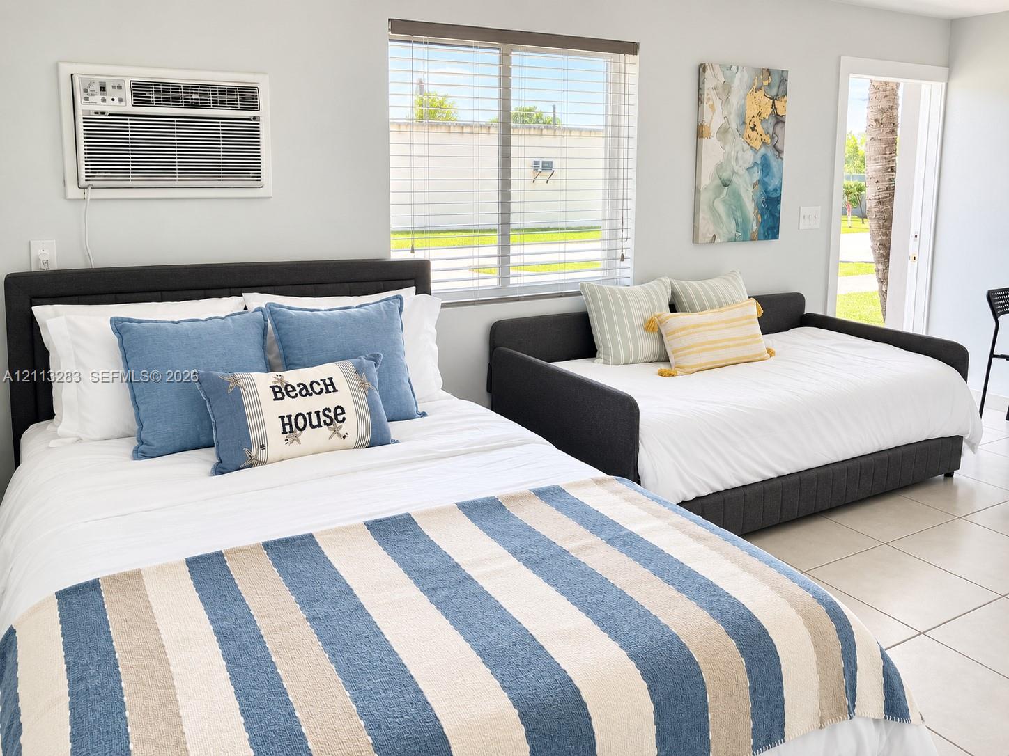 Neutral-toned tile flooring, large windows with horizontal blinds, and a wall-mounted air conditioning unit