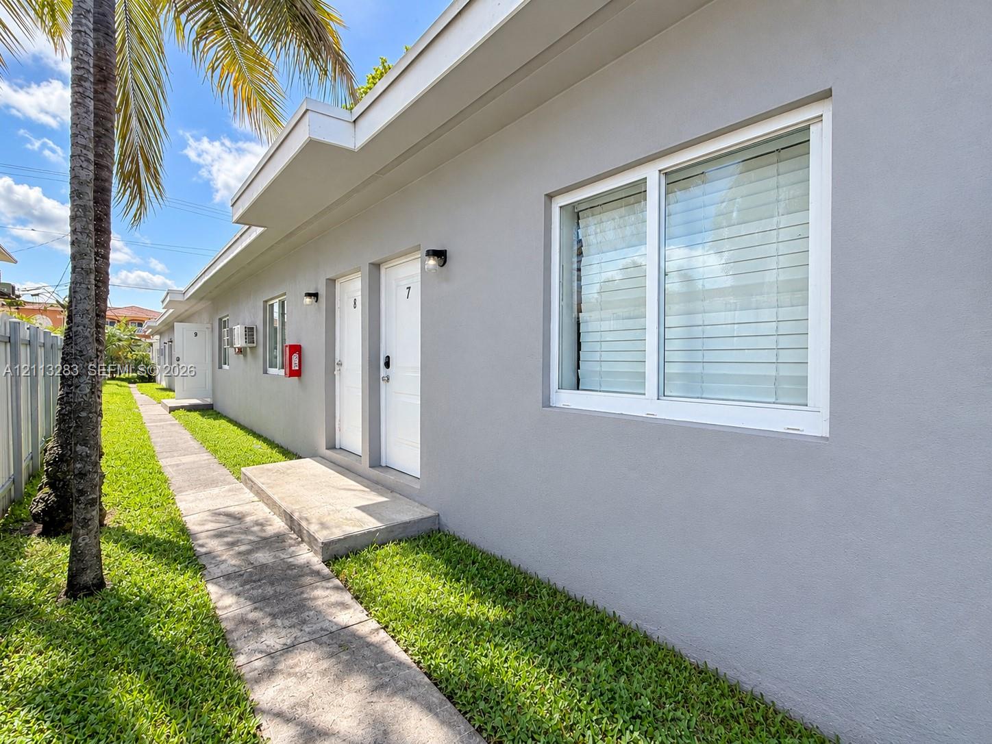 Exterior featuring smooth gray stucco facade, white-trimmed dual-pane windows, concrete walkways, and manicured lawn Exterior featuring smooth gray stucco facade, white-trimmed dual-pane windows, concrete walkways, and manicured lawn