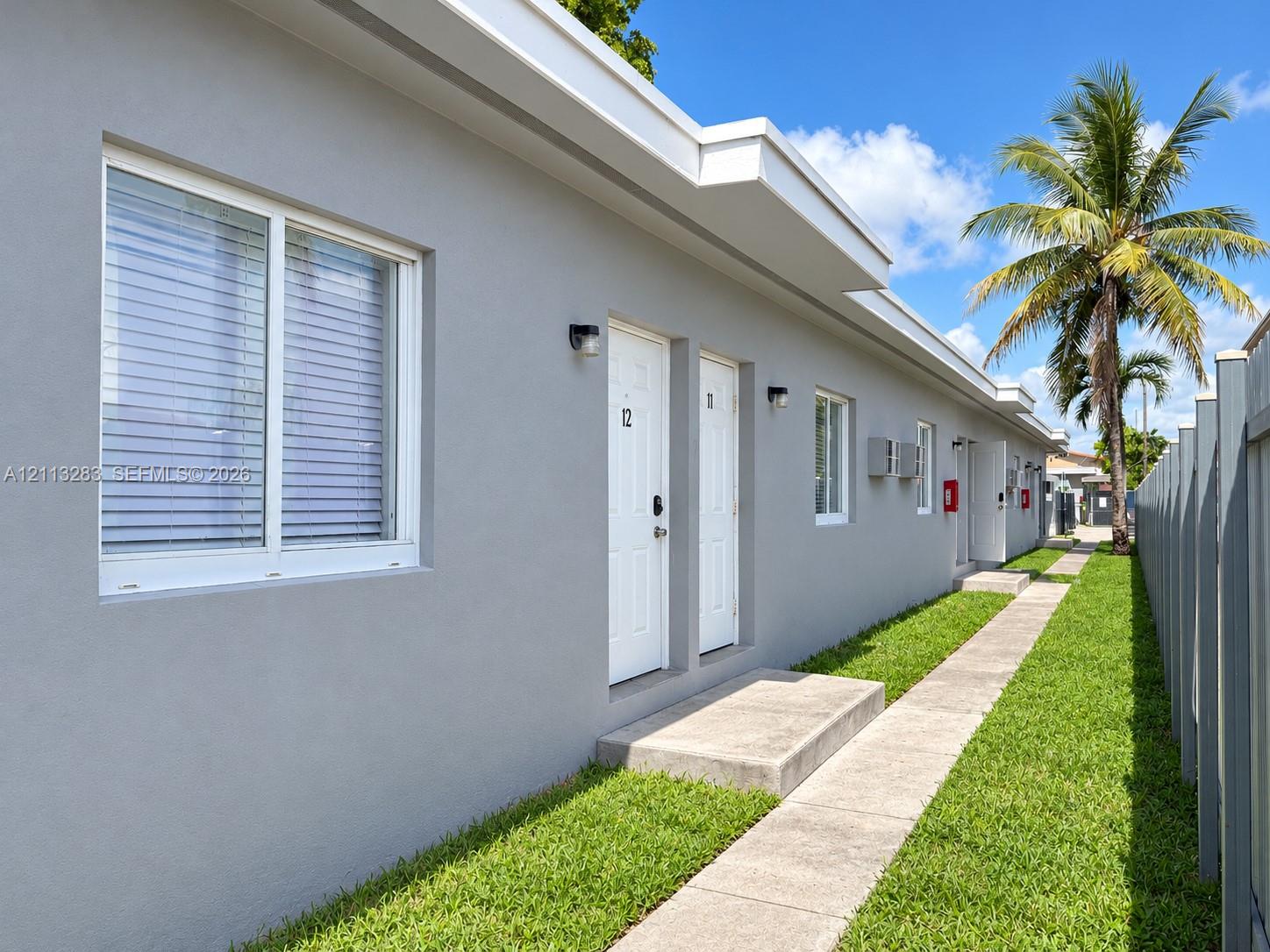 Stucco exterior featuring dual-pane sliding windows, concrete entry steps, wall-mounted exterior lighting, and a paved walkway bordered by manicured lawn Stucco exterior featuring dual-pane sliding windows, concrete entry steps, wall-mounted exterior lighting, and a paved walkway bordered by manicured lawn