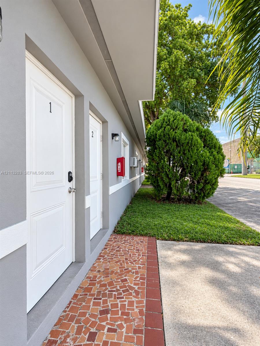 Exterior facade featuring smooth grey stucco, white-trimmed door frames, mosaic tile walkway with brick edging, and manicured landscaping Exterior facade featuring smooth grey stucco, white-trimmed door frames, mosaic tile walkway with brick edging, and manicured landscaping