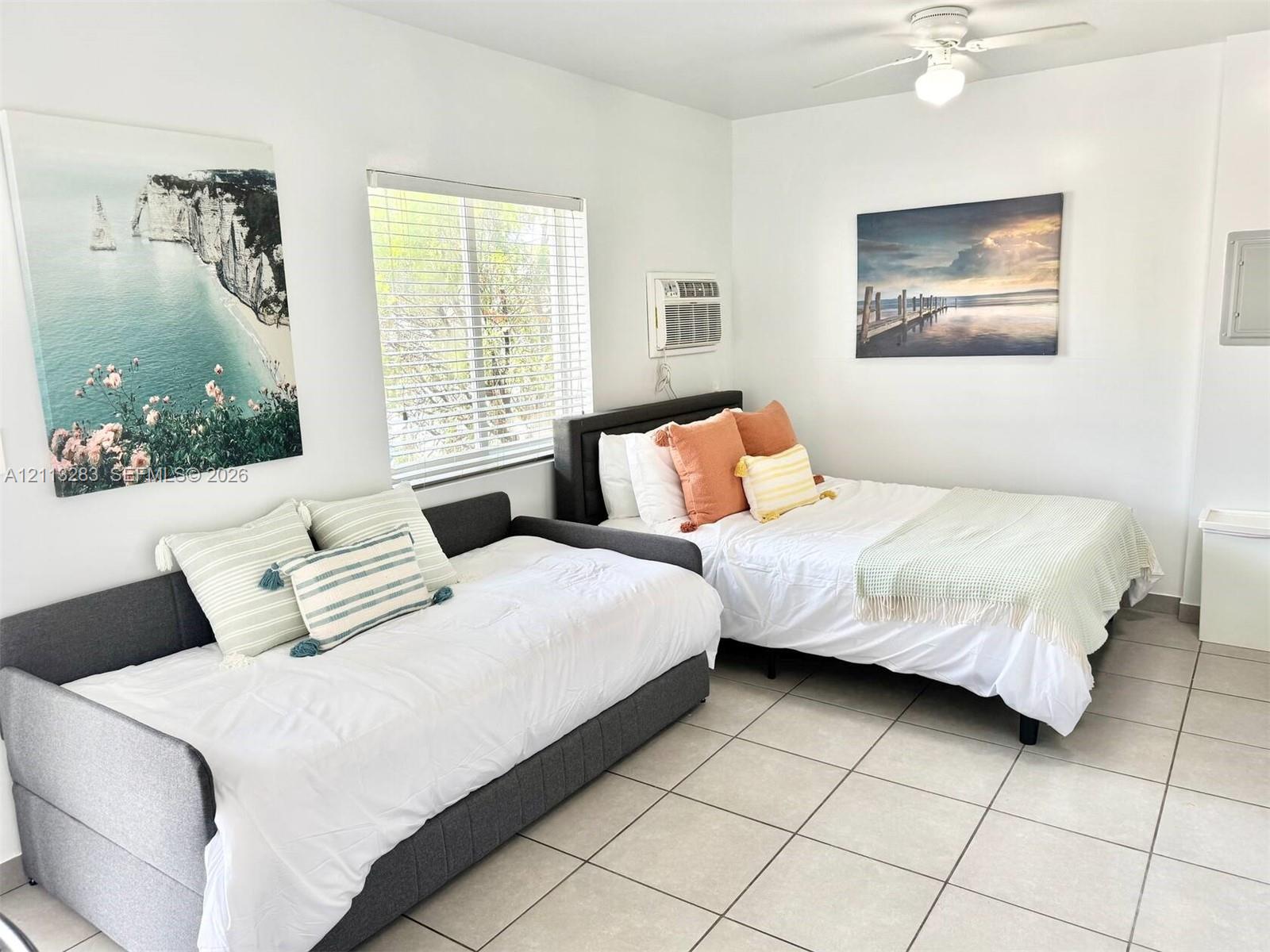 Light-filled room featuring neutral ceramic tile flooring, a wall-mounted climate control unit, and a ceiling-mounted light fixture with an integrated fan Light-filled room featuring neutral ceramic tile flooring, a wall-mounted climate control unit, and a ceiling-mounted light fixture with an integrated fan