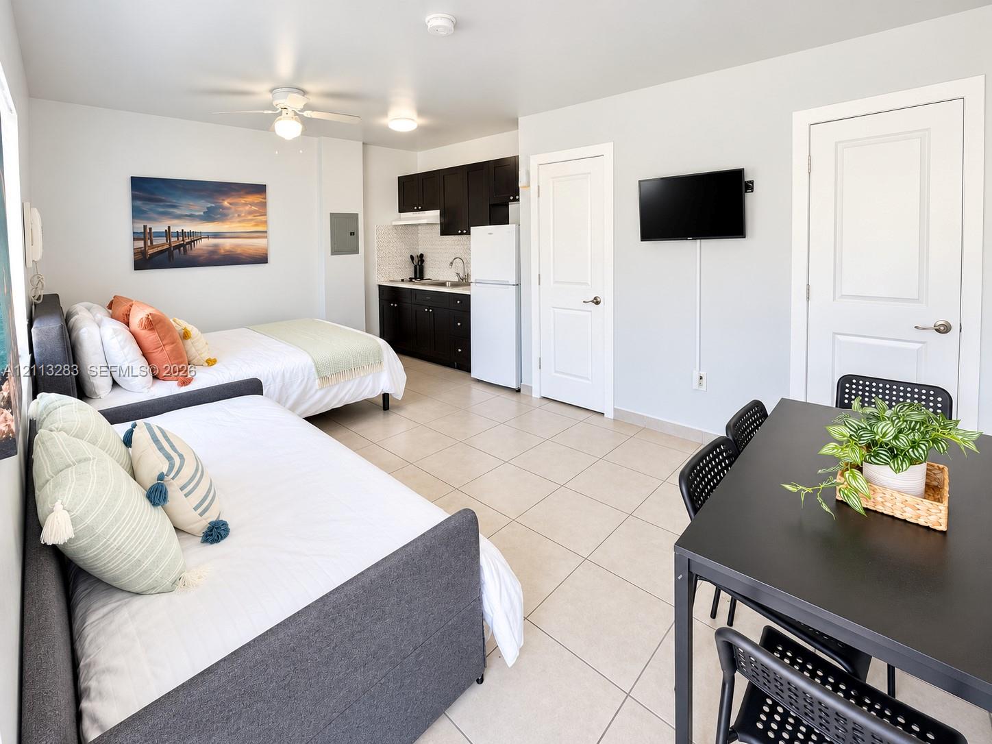 Studio space featuring neutral ceramic tile flooring, kitchen cabinetry with a dark finish, ceiling fan, and two-panel interior doors