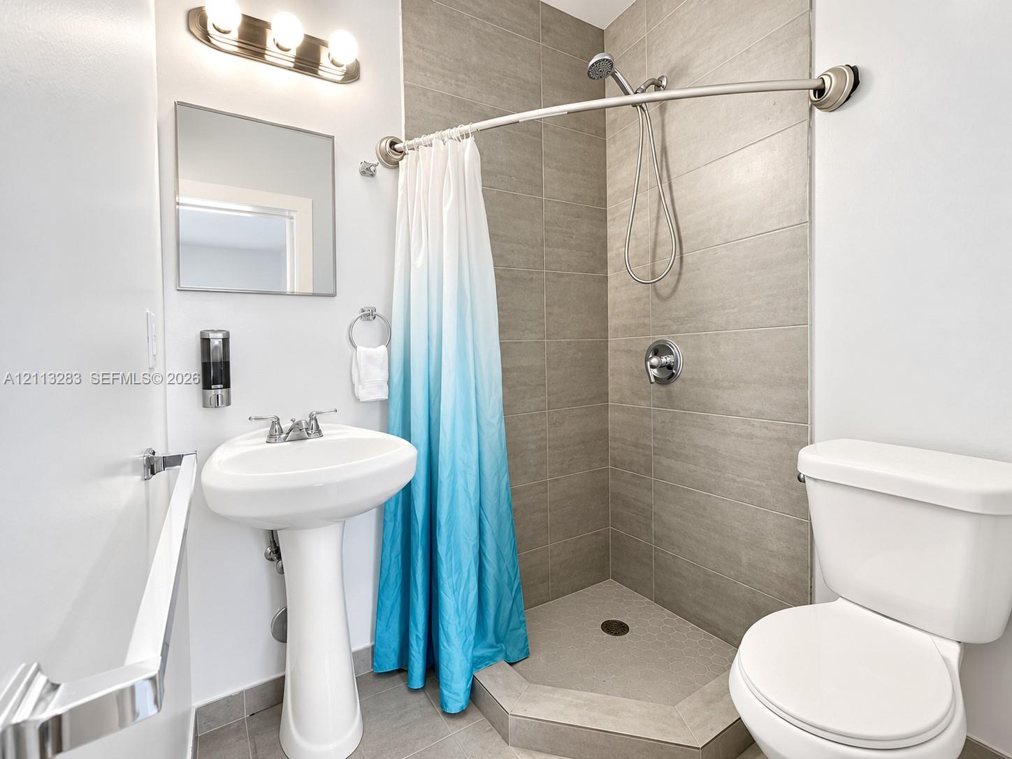 Bathroom featuring a pedestal sink, brushed-nickel hardware, large-format tile shower surround, and a walk-in shower with a curved shower rod