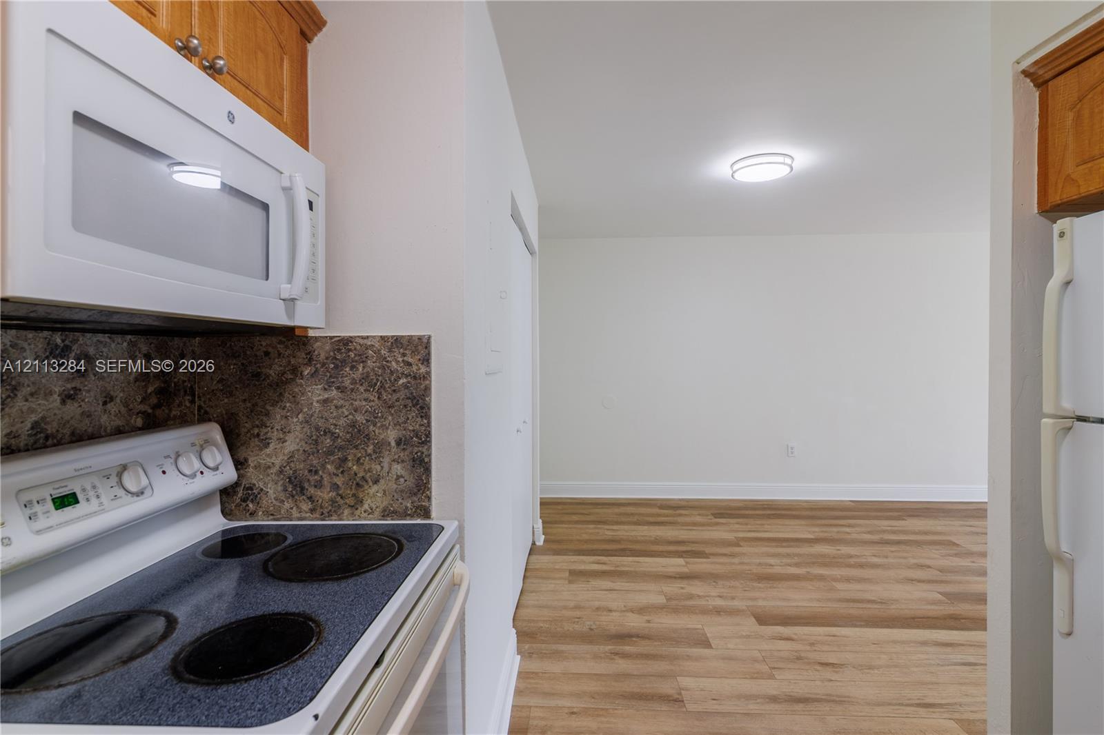 Kitchen featuring wood-finish cabinetry, an over-the-range microwave, electric range, wood-finish flooring, and a textured backsplash
