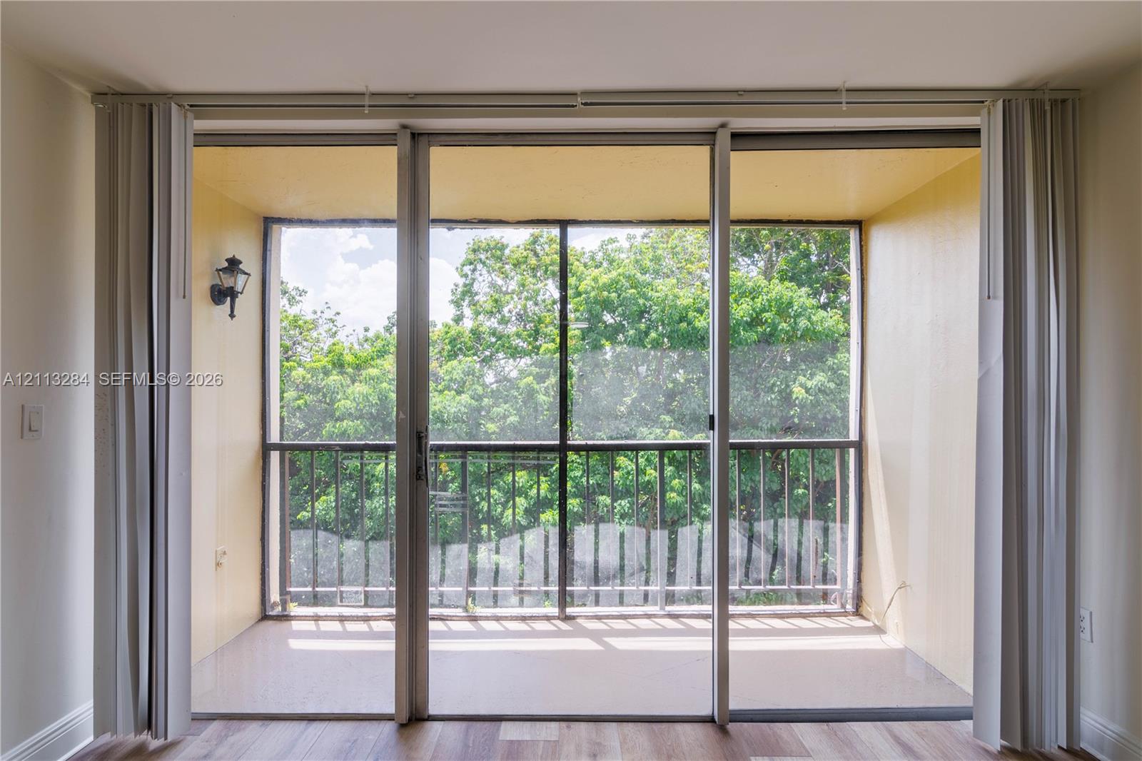 Screened-in balcony featuring metal railing, wall-mounted exterior lighting, and wood-finish flooring, accessed by floor-to-ceiling sliding glass doors