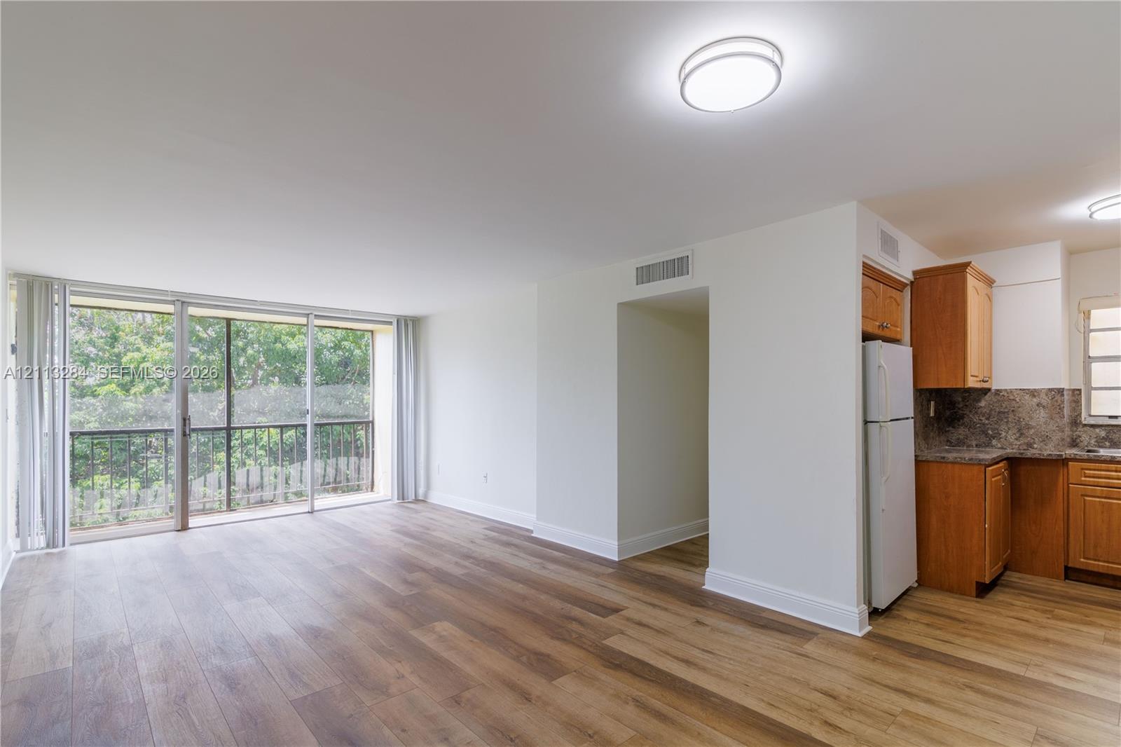 Wood-finish flooring, sliding glass door with balcony access, wood cabinetry, and flush-mount lighting fixtures