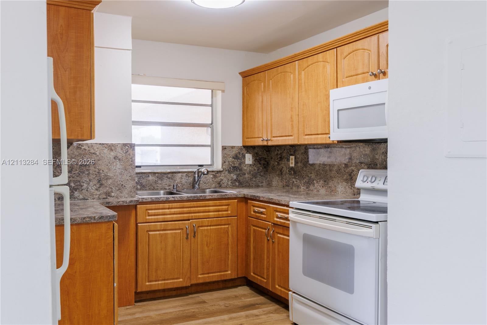 Kitchen featuring wood cabinetry, laminate countertops with coordinating backsplash, integrated white appliances, and wood-finish flooring