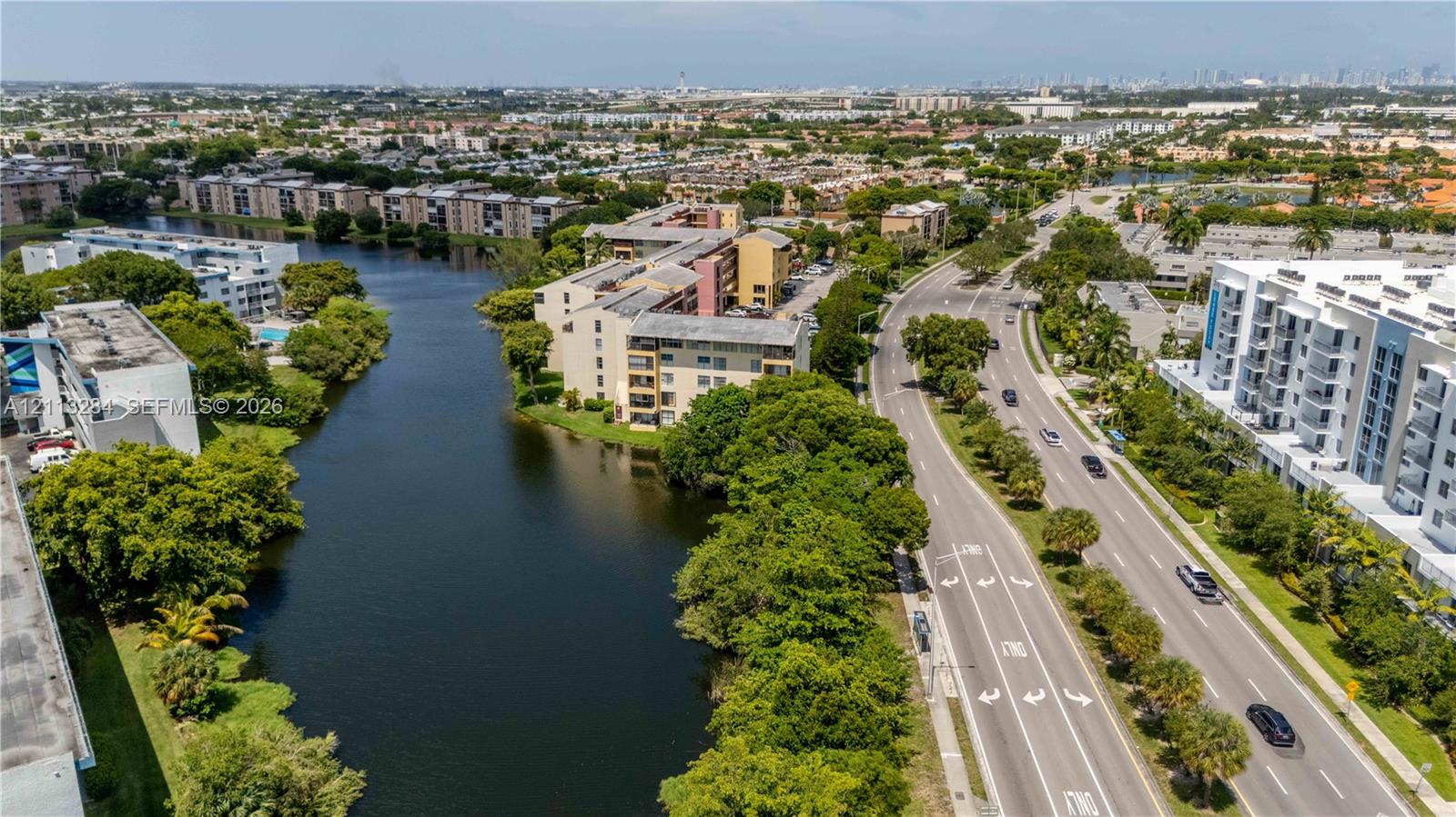Aerial perspective featuring a multi-story residential building complex, a linear canal, and surrounding mature tree canopy