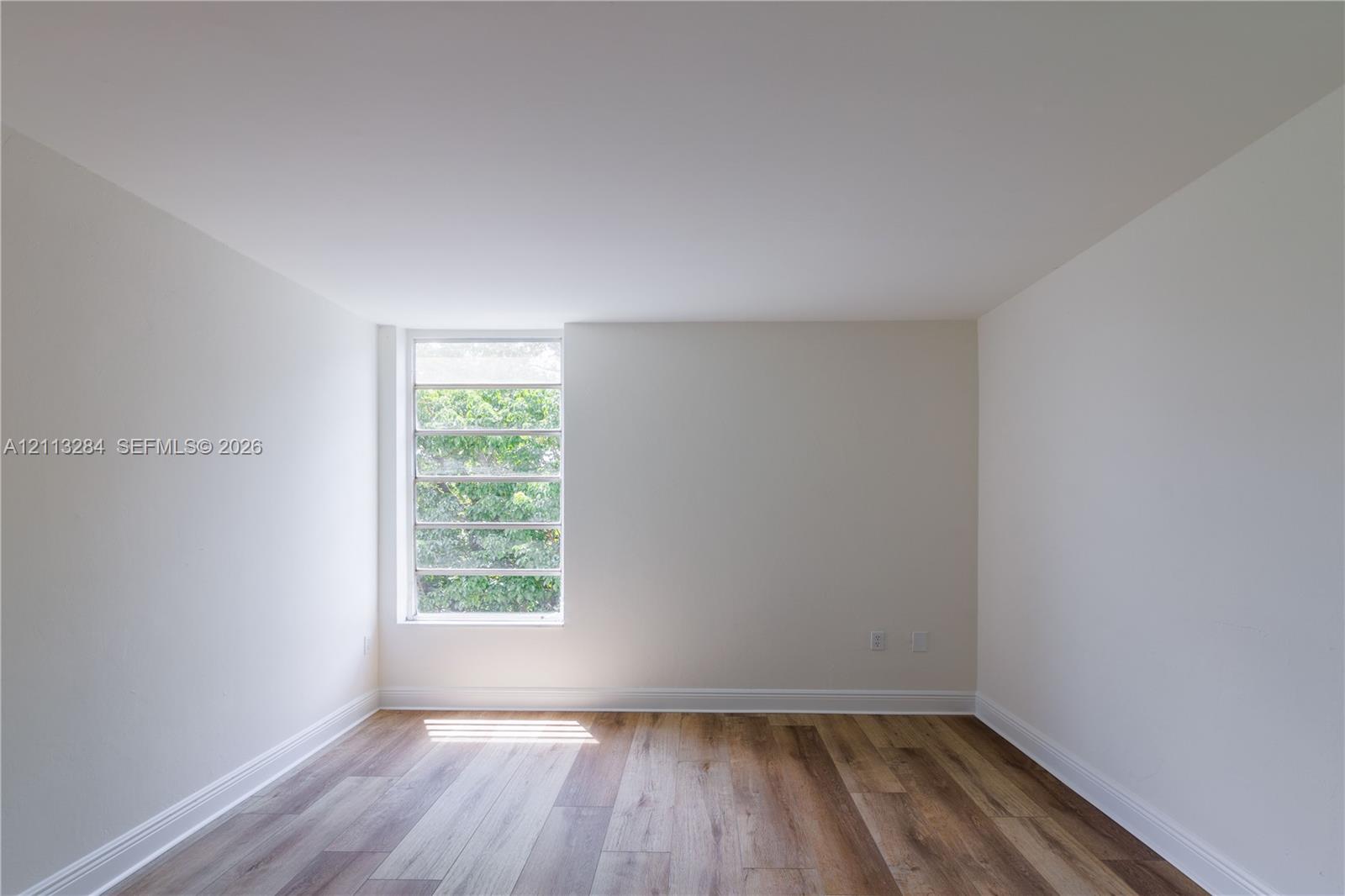 Room featuring wood-finish flooring, crisp neutral walls, and a multi-pane window
