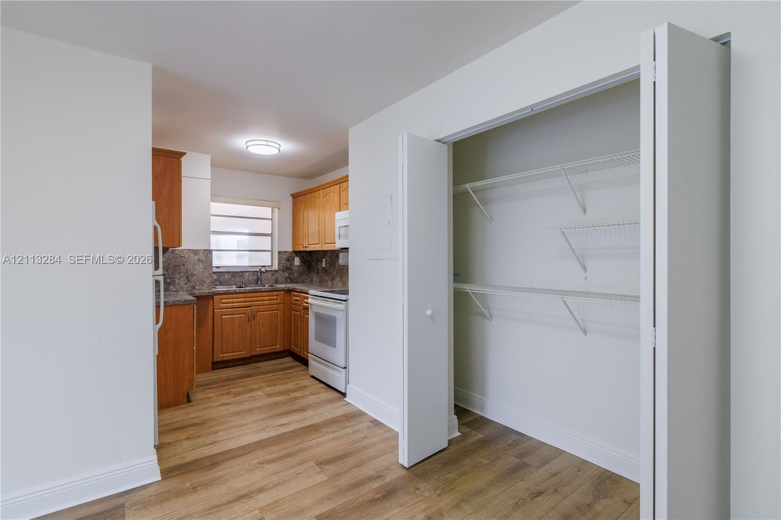 Kitchen featuring wood-finish cabinetry, stone-texture countertops, white appliances, and wood-finish flooring, complemented by a walk-in closet with white wire shelving