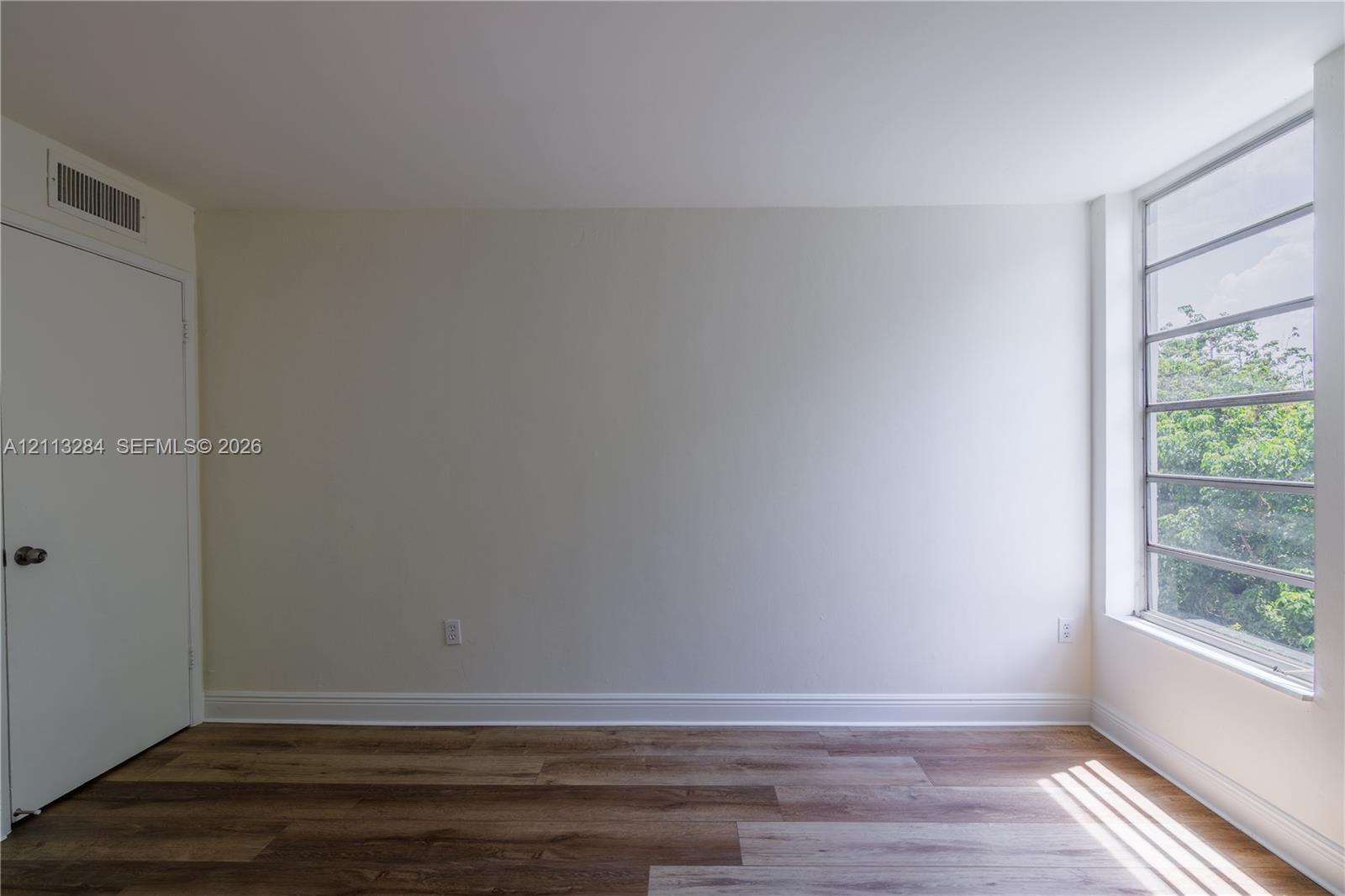 Neutral interior space featuring wood-finish flooring, a multi-pane window, and a white interior door