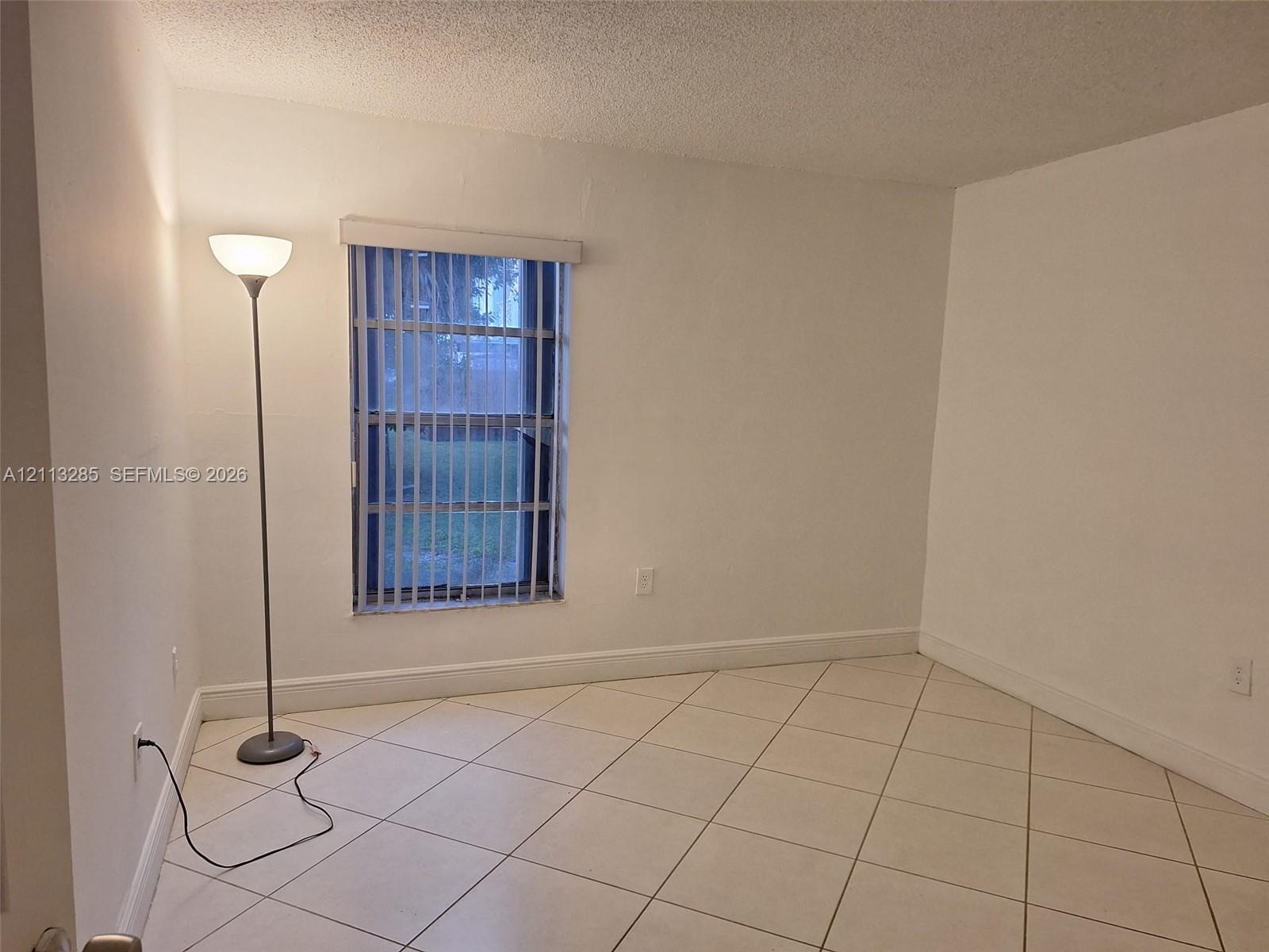 Interior room featuring neutral wall-to-wall ceramic tile flooring set on a diagonal pattern and a single window with vertical blinds Interior room featuring neutral wall-to-wall ceramic tile flooring set on a diagonal pattern and a single window with vertical blinds