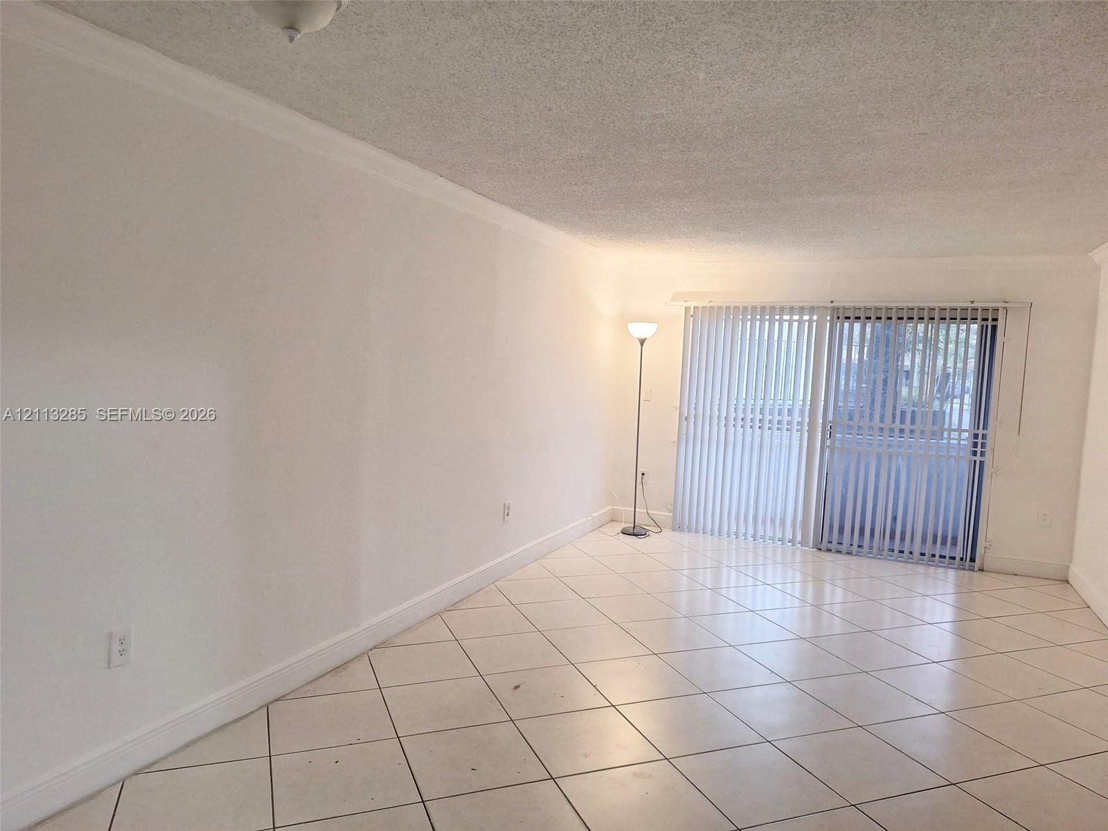 Interior space featuring large-format diagonal tile flooring, smooth wall finishes, and glass sliding doors with vertical blinds Interior space featuring large-format diagonal tile flooring, smooth wall finishes, and glass sliding doors with vertical blinds