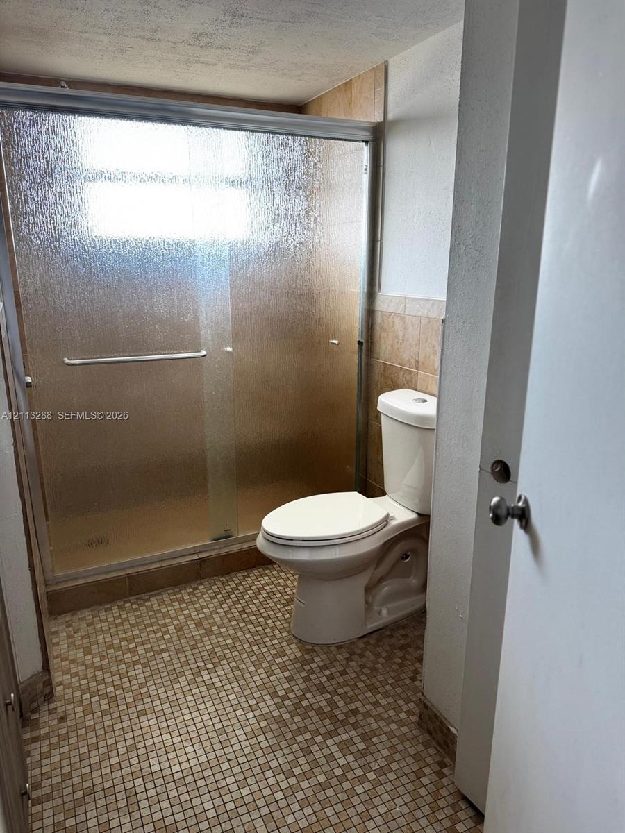 Bathroom featuring a glass-enclosed shower, mosaic tile flooring, and neutral wall tile surround Bathroom featuring a glass-enclosed shower, mosaic tile flooring, and neutral wall tile surround