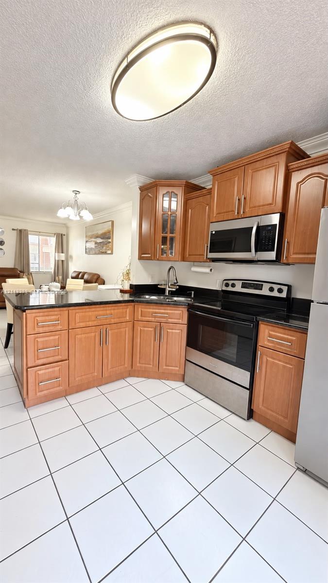 Kitchen featuring wood cabinetry, stone countertops, stainless steel appliances, ceramic tile flooring, and a flush-mount overhead light fixture