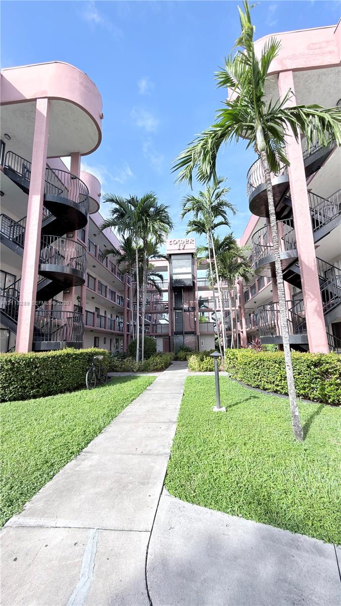 Multi-story residential complex featuring curved architectural elements, wrought iron spiral staircases, central concrete walkway, mature palm trees, and manicured landscaping