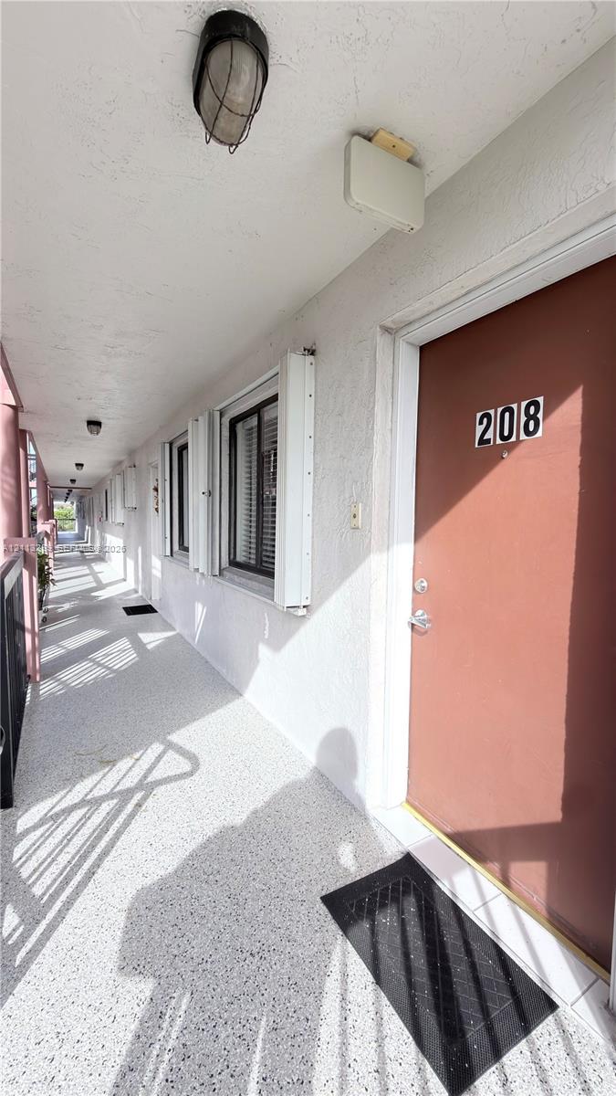 Exterior entryway featuring a textured concrete walkway, solid-core entrance door, and recessed wall-mounted lighting fixtures