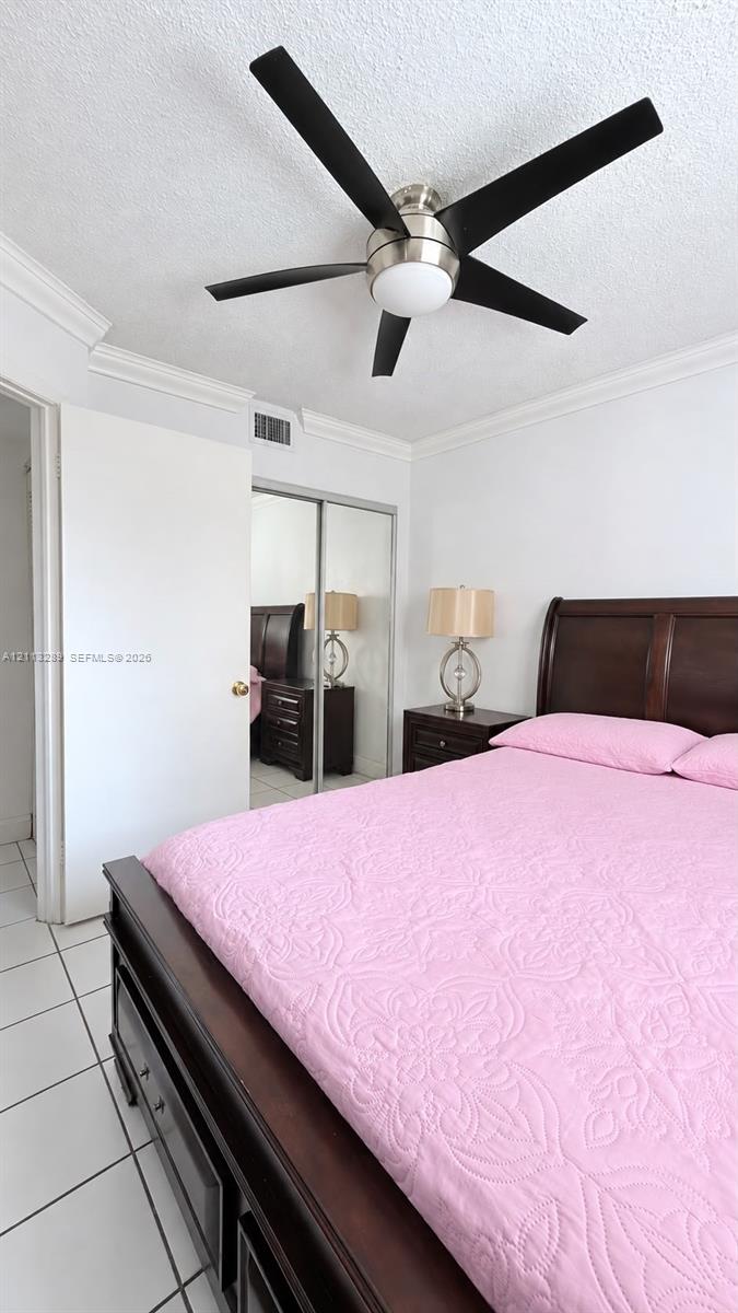 Room featuring white ceramic tile flooring, crown molding, a brushed nickel and black ceiling fan with integrated lighting, and a closet with mirrored sliding doors
