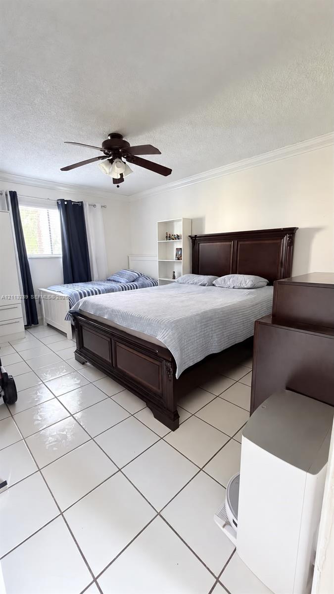 Room featuring tile flooring, ceiling fan with integrated lighting, and crown molding
