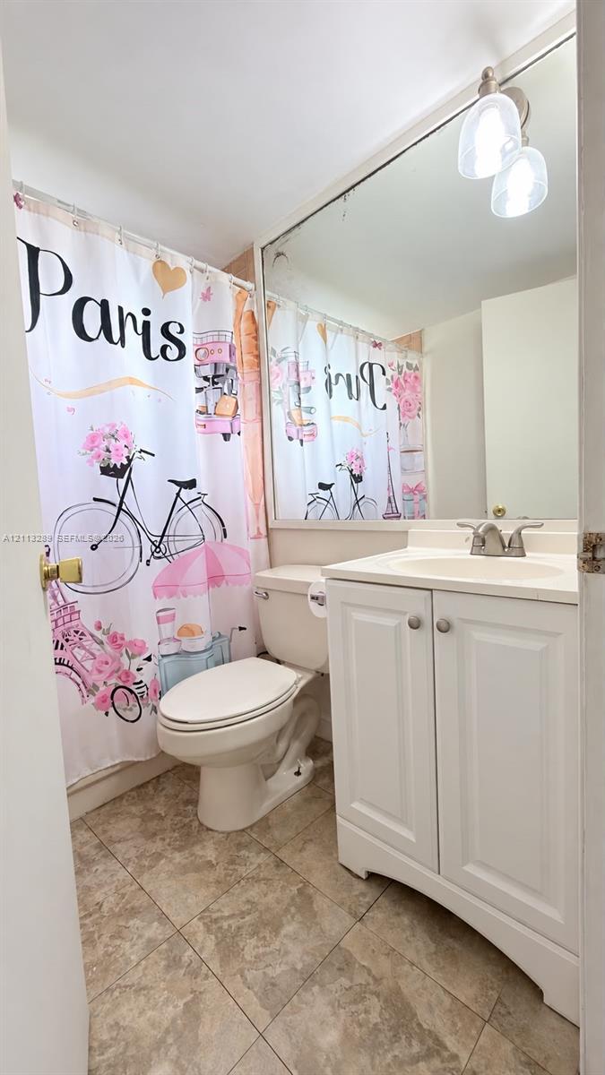Bathroom featuring a white vanity cabinet, integrated sink, dual-handle faucet, large wall-mounted mirror, and tile flooring