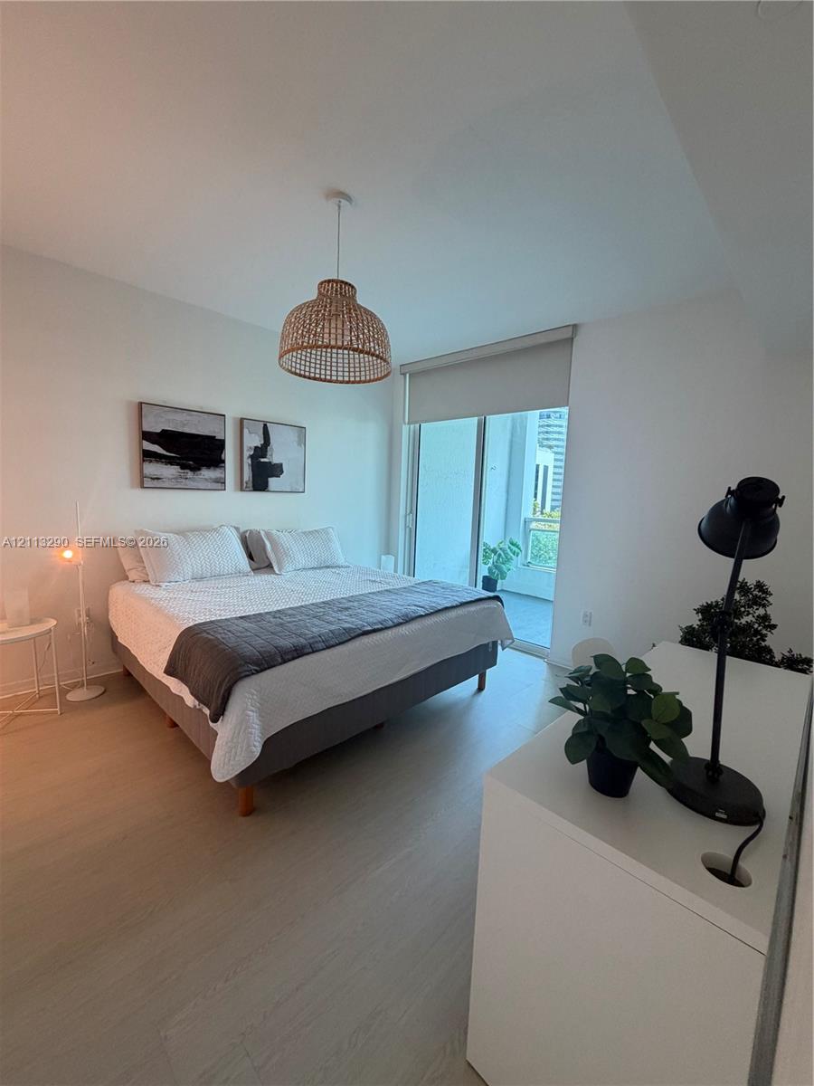 Light-toned wood-finish flooring, textured woven pendant lighting, floor-to-ceiling glass sliding doors, and access to a private balcony