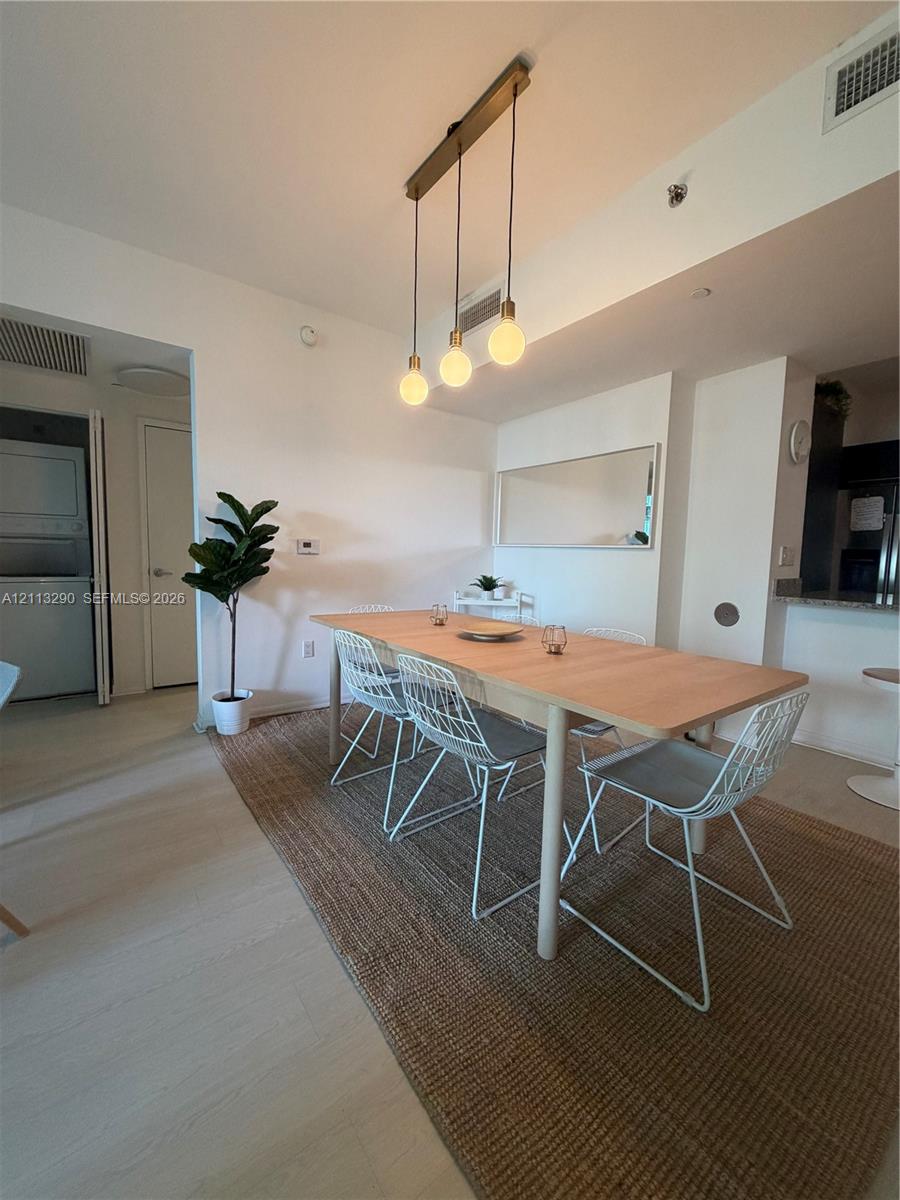 Multi-pendant linear light fixture with exposed bulbs, neutral wood-finish flooring, and wall-mounted mirror Multi-pendant linear light fixture with exposed bulbs, neutral wood-finish flooring, and wall-mounted mirror
