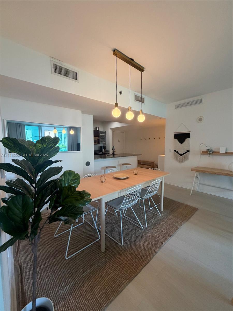 Open-concept interior featuring light-toned wood-finish flooring, a linear three-pendant light fixture, and a built-in wall shelf Open-concept interior featuring light-toned wood-finish flooring, a linear three-pendant light fixture, and a built-in wall shelf