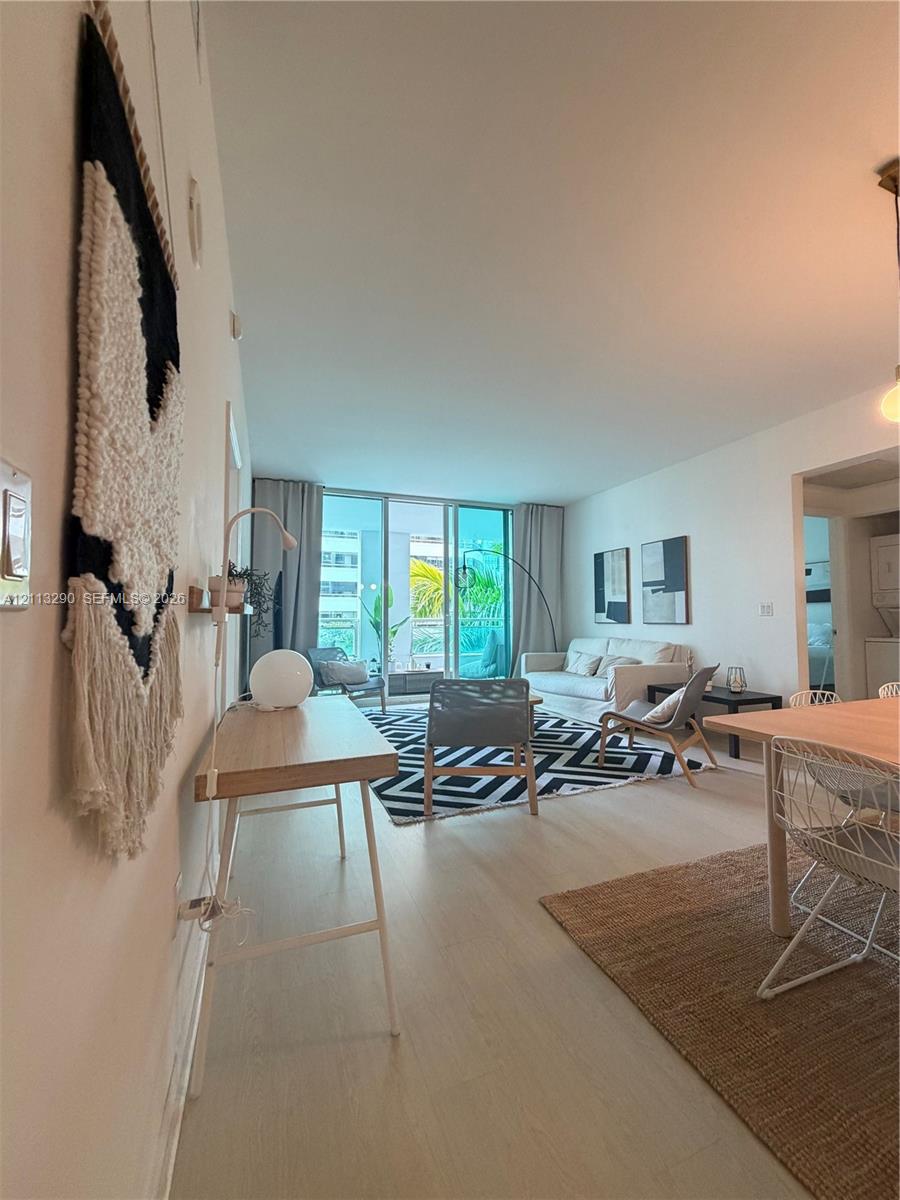 Open-concept interior featuring wood-finish flooring, high ceilings, and floor-to-ceiling glass doors providing access to a balcony Open-concept interior featuring wood-finish flooring, high ceilings, and floor-to-ceiling glass doors providing access to a balcony