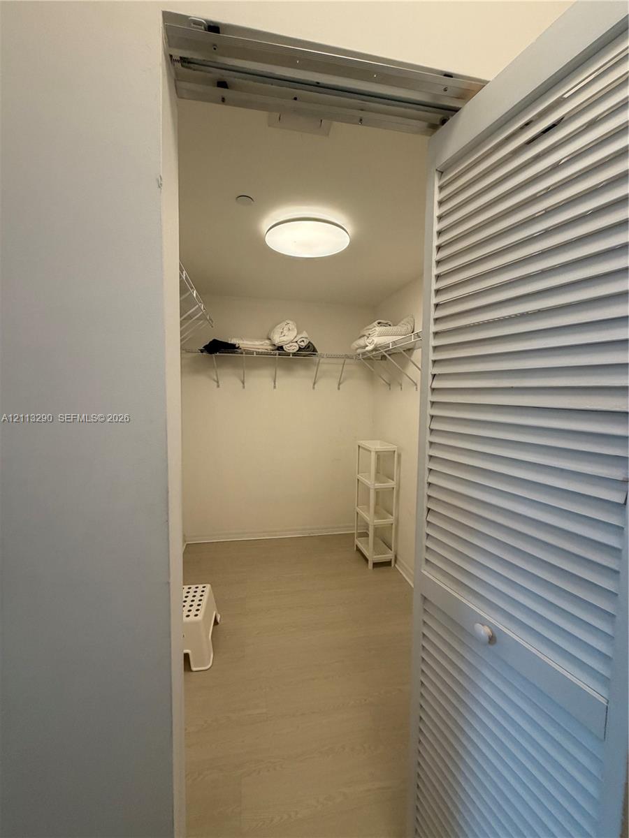 Storage closet featuring white louvered doors, neutral wood-finish flooring, and built-in wire shelving