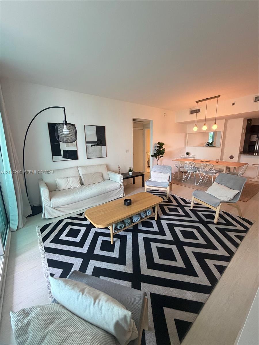 Open-concept interior featuring wood-finish flooring, recessed lighting, and a linear three-pendant light fixture over the dining area Open-concept interior featuring wood-finish flooring, recessed lighting, and a linear three-pendant light fixture over the dining area