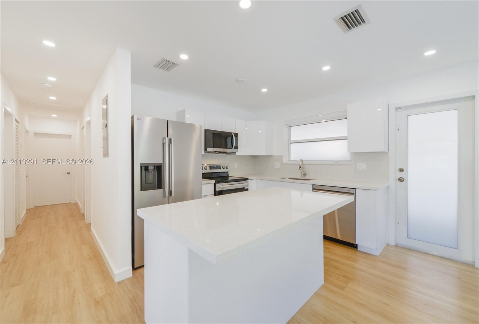 Kitchen featuring white flat-panel cabinetry, a central island with a quartz countertop, stainless steel appliances, and wood-finish flooring