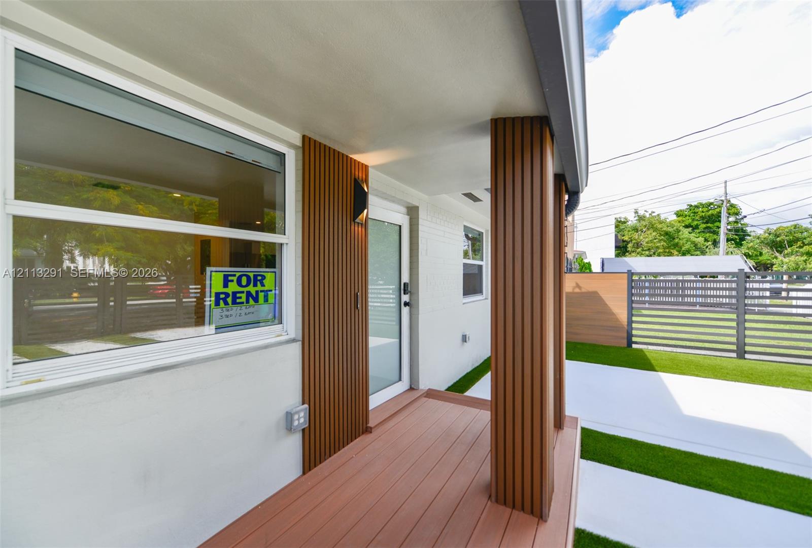 Covered entryway featuring wood-finish decking, vertical slat accents, a structural column, and a modern exterior light fixture Covered entryway featuring wood-finish decking, vertical slat accents, a structural column, and a modern exterior light fixture