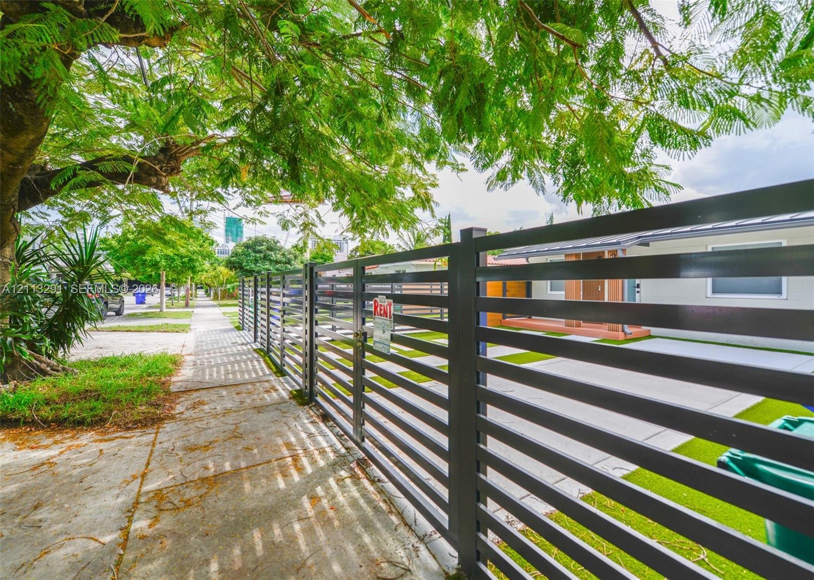 Horizontal slat metal fencing, gated entry, concrete driveway, and mature landscaping Horizontal slat metal fencing, gated entry, concrete driveway, and mature landscaping