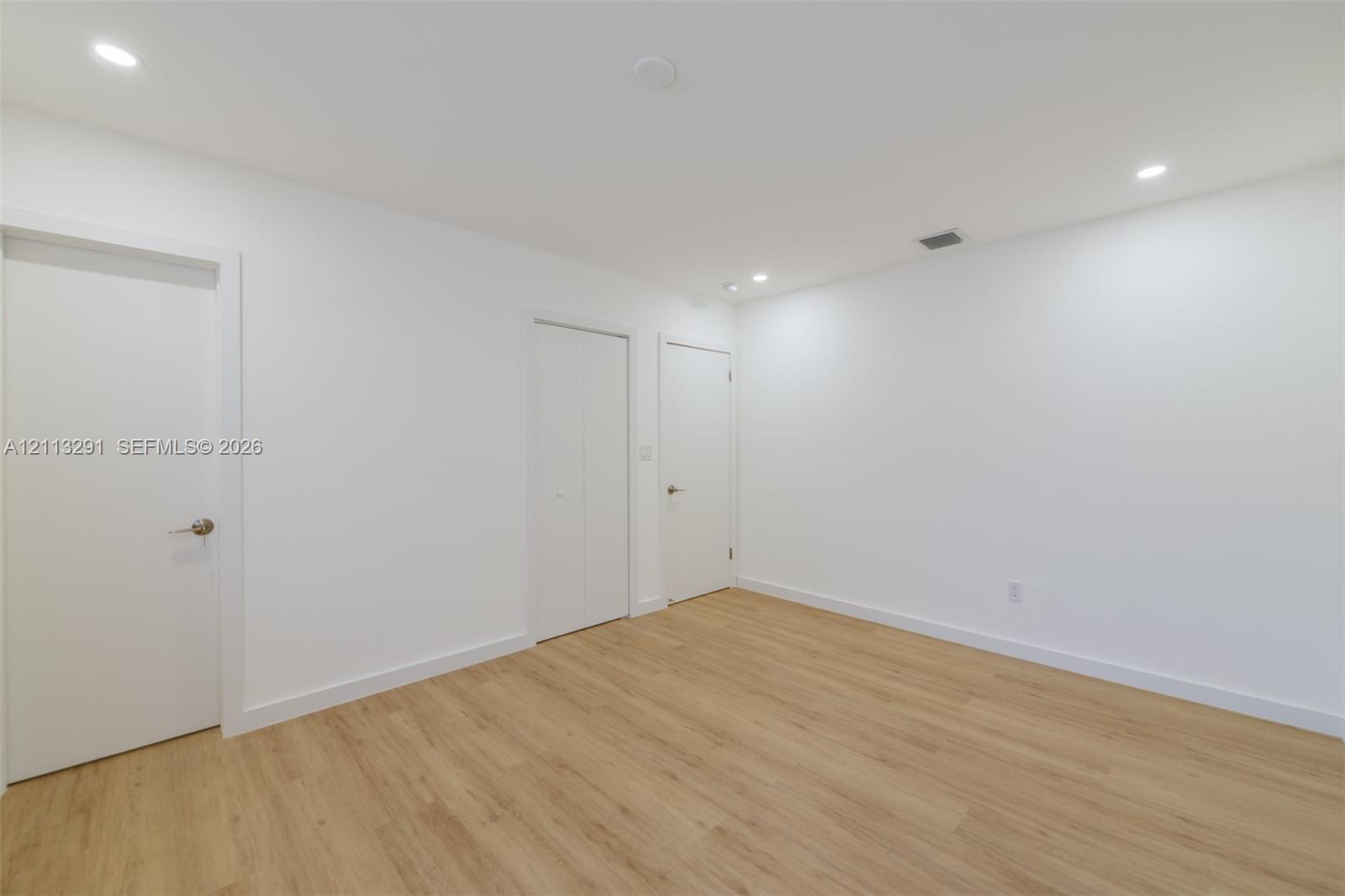 Interior room featuring wood-finish flooring, recessed lighting, and multiple interior doors with satin nickel hardware